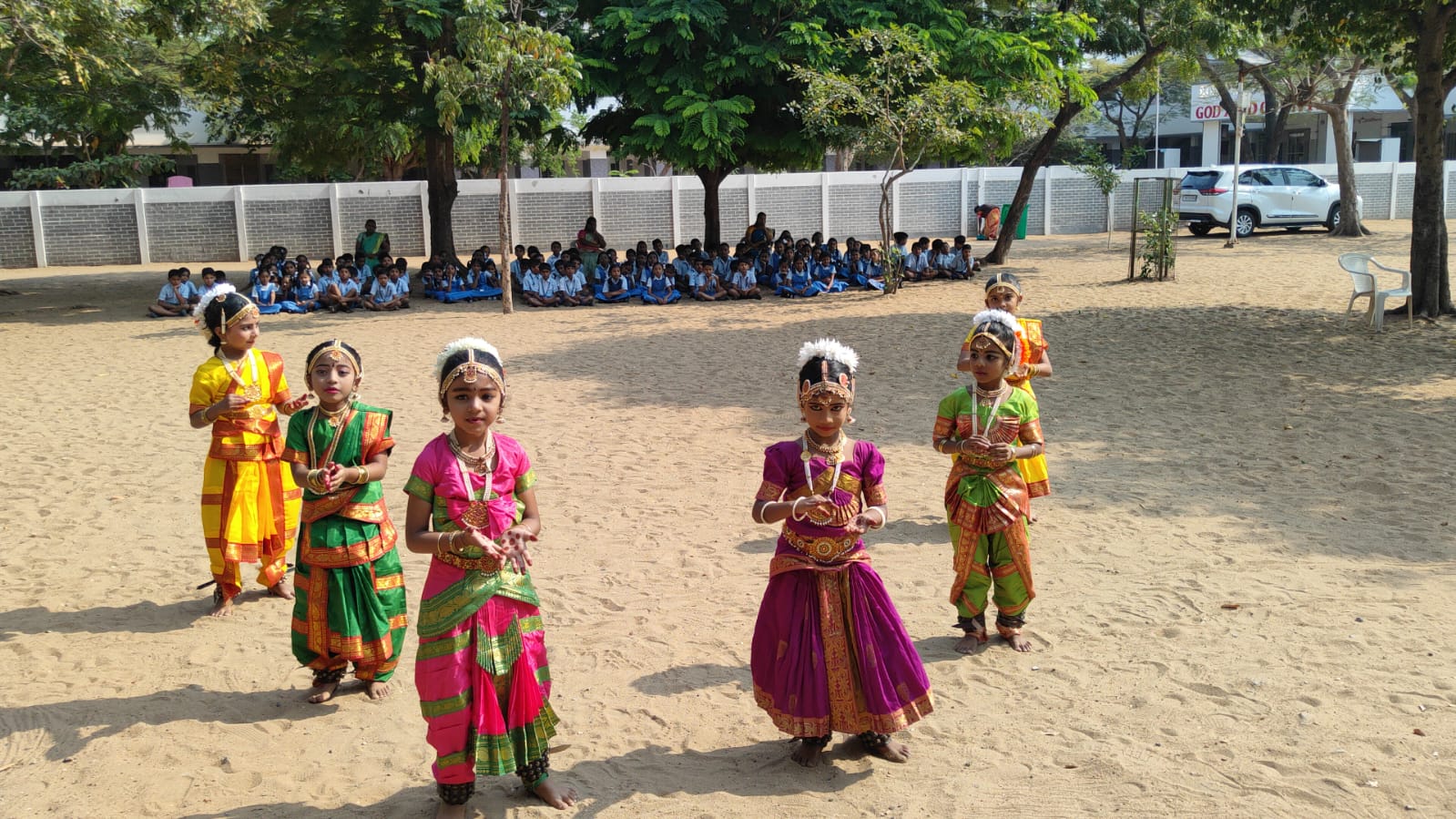 Children in classical dance costume performing on the school ground while the whole school watches